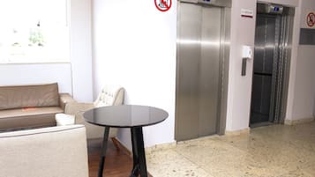 Um hall com sofá, uma mesa redonda e dois elevadores.