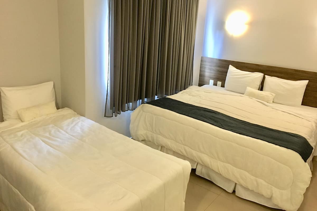 Ein Hotelzimmer mit zwei Betten, einem großen Fenster mit Vorhängen, einem Holz-Kopfteil und einer Wandleuchte.