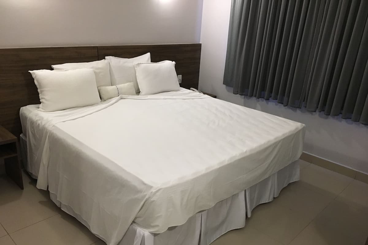 Ein großes Bett mit weißer Bettwäsche, einem Holz-Kopfteil und einem grauen Vorhang.