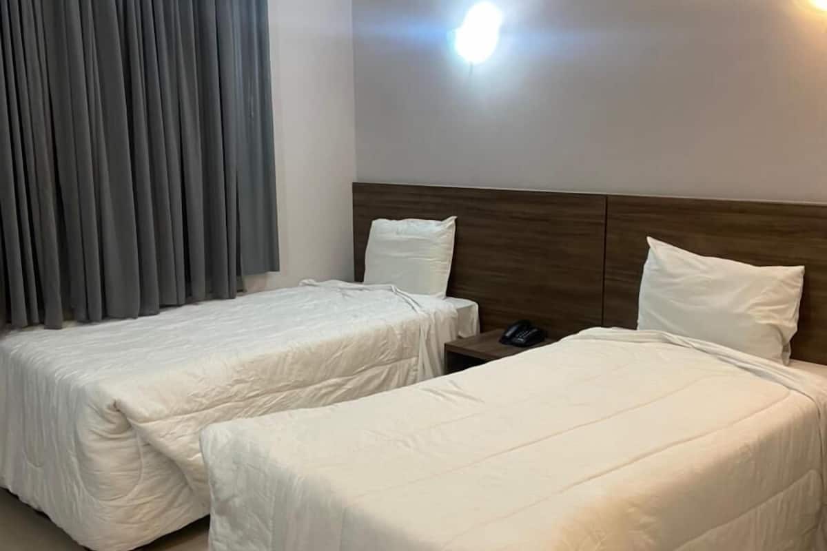 Ein Hotelzimmer mit zwei Einzelbetten, einem Holzkopfteil, einem Nachttischtelefon und einer Wandleuchte.