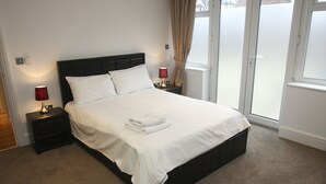 A neatly made bed with white linens, two bedside tables with lamps, and a view of the outdoors through a sliding door. - 2 Bed Apt in Chorleywood Near Station (Rickmansworth)