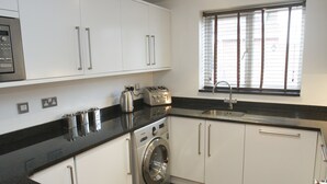 A modern kitchen with white cabinets, a built-in washing machine, a toaster, and a window with blinds. - 2 Bed Apt in Chorleywood Near Station (Rickmansworth)