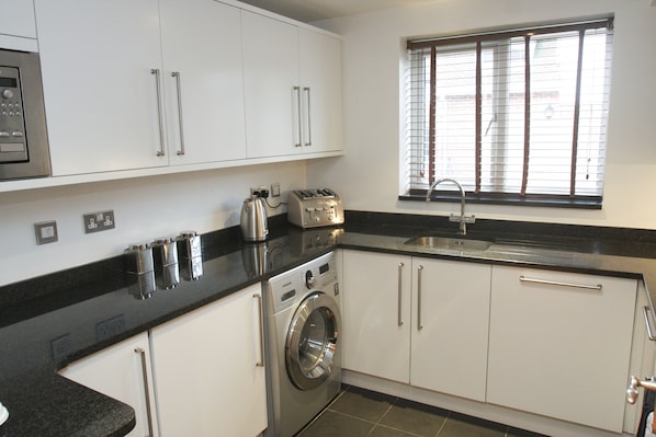 A modern kitchen with white cabinets, a built-in washing machine, a toaster, and a window with blinds.