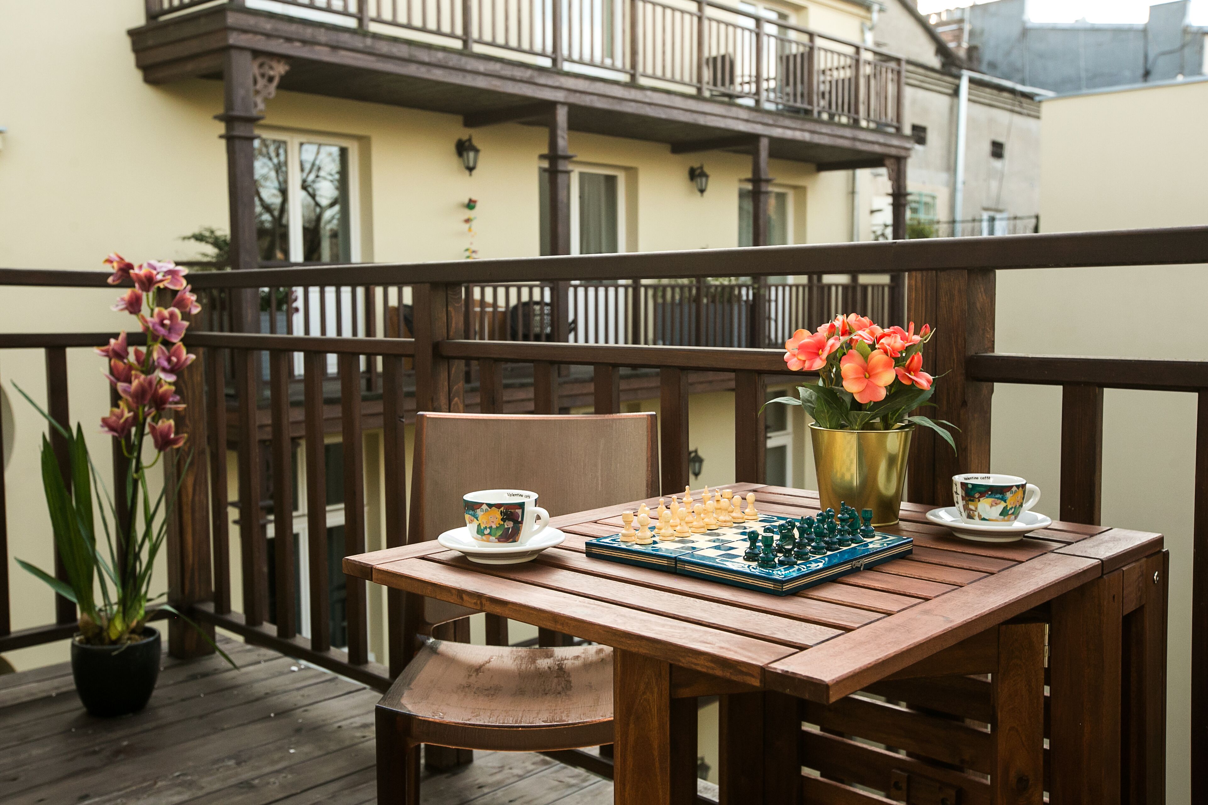 A wooden table with chess set and two cups on a balcony.
