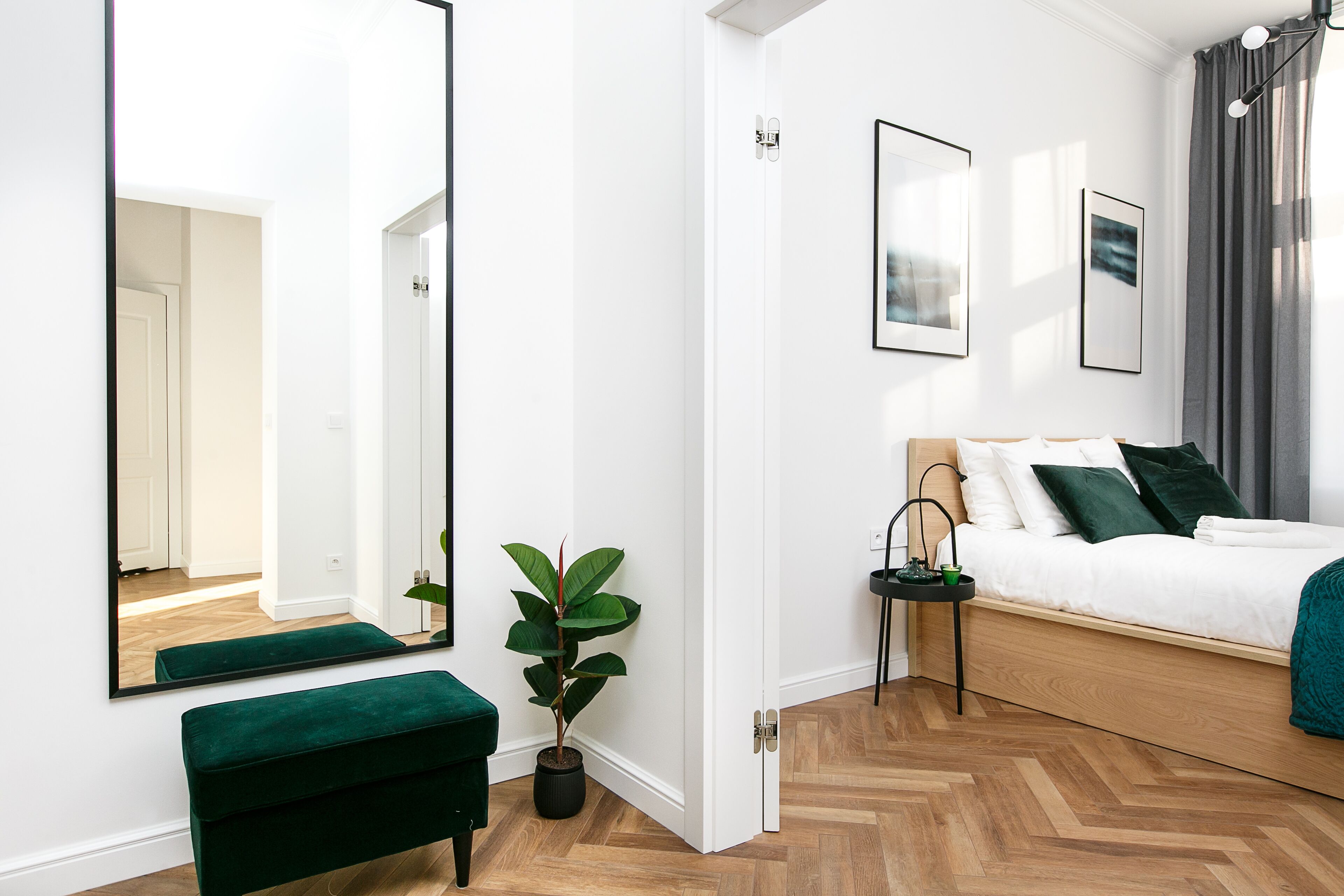 A modern bedroom with a wooden bed, a green bench, a potted plant, and a large mirror.
