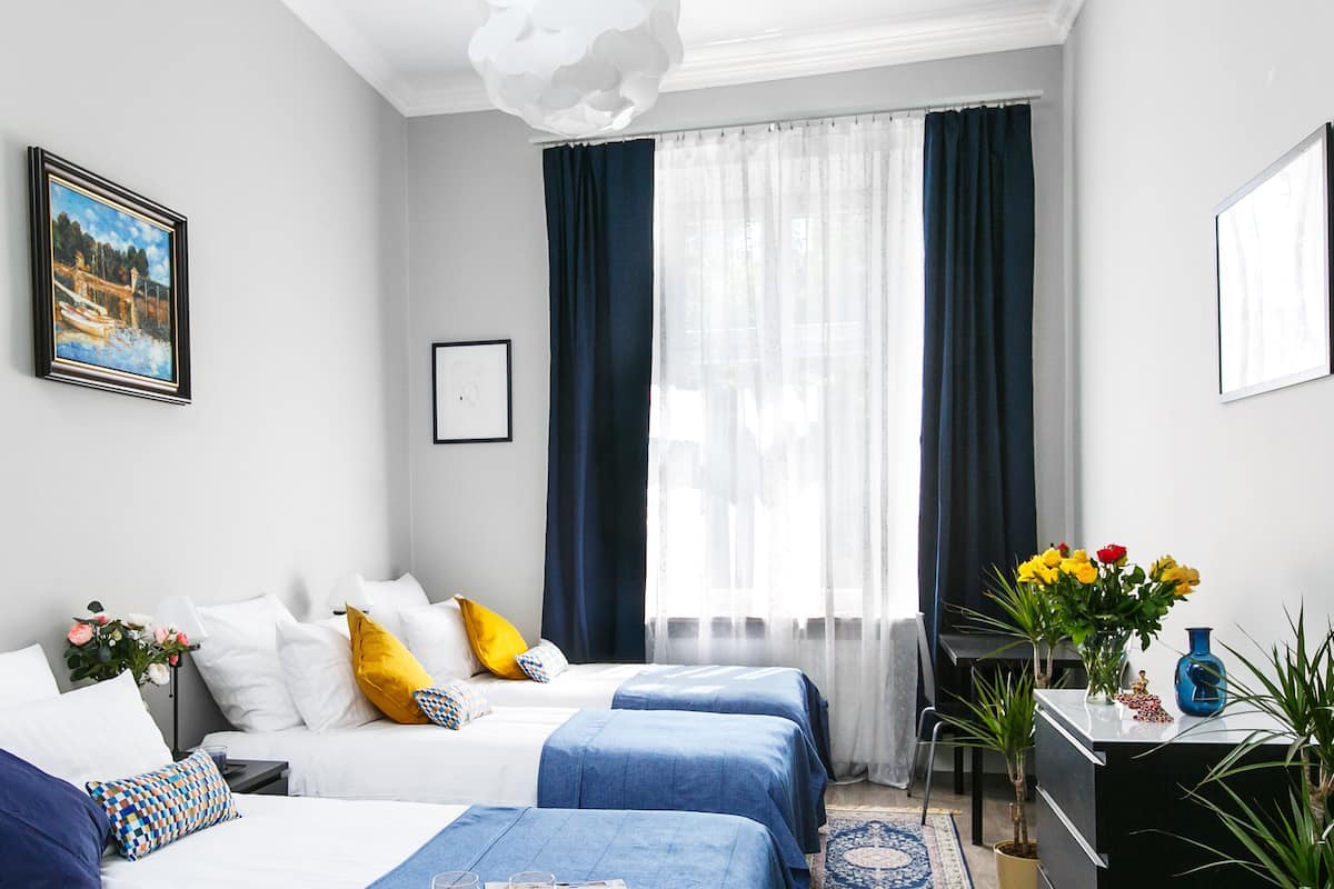 Ein Hotelzimmer mit zwei Betten, einem Schreibtisch, einem Stuhl, einem Fenster mit Vorhängen, einem Gemälde und einer Vase mit Blumen.
