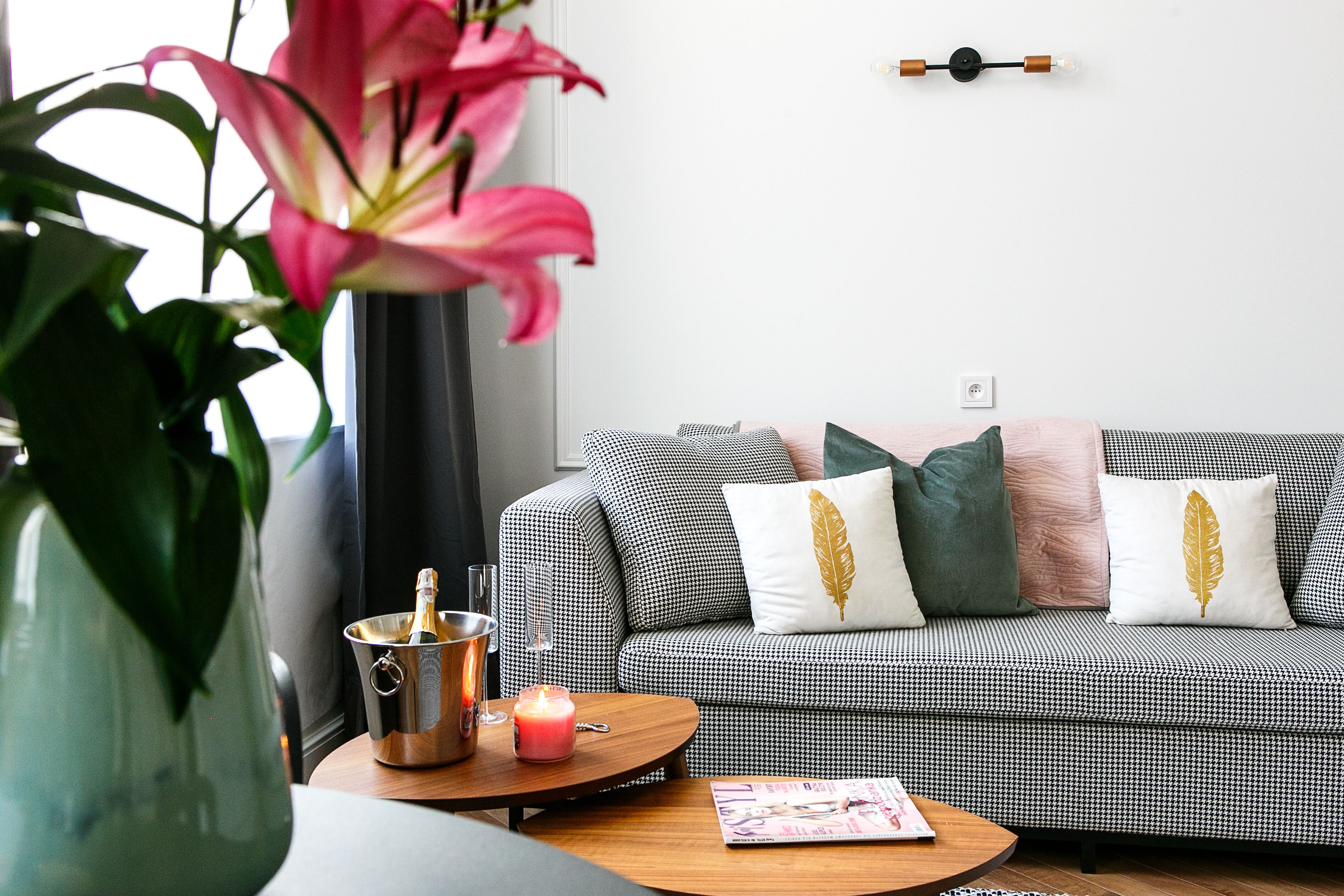 A cozy living room with a checkered sofa, a wooden coffee table, a vase with a plant, and a candle on the table.
