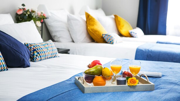 A neatly made bed with a tray of fruit and juice, a remote control, and a flower on a blue bedspread. - Otium Old Town Sarego (Kraków)
