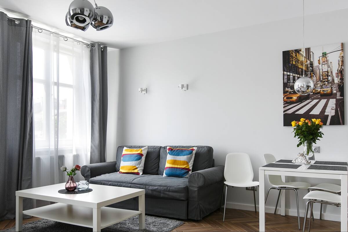 Ein modernes Wohnzimmer mit grauem Sofa, weißem Couchtisch und einem Essbereich mit weißem Tisch und Stühlen.