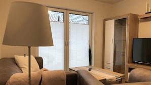 A living room with a sofa, a coffee table, a lamp, a television, and a cabinet. - Ferienpark Thüle (Friesoythe)