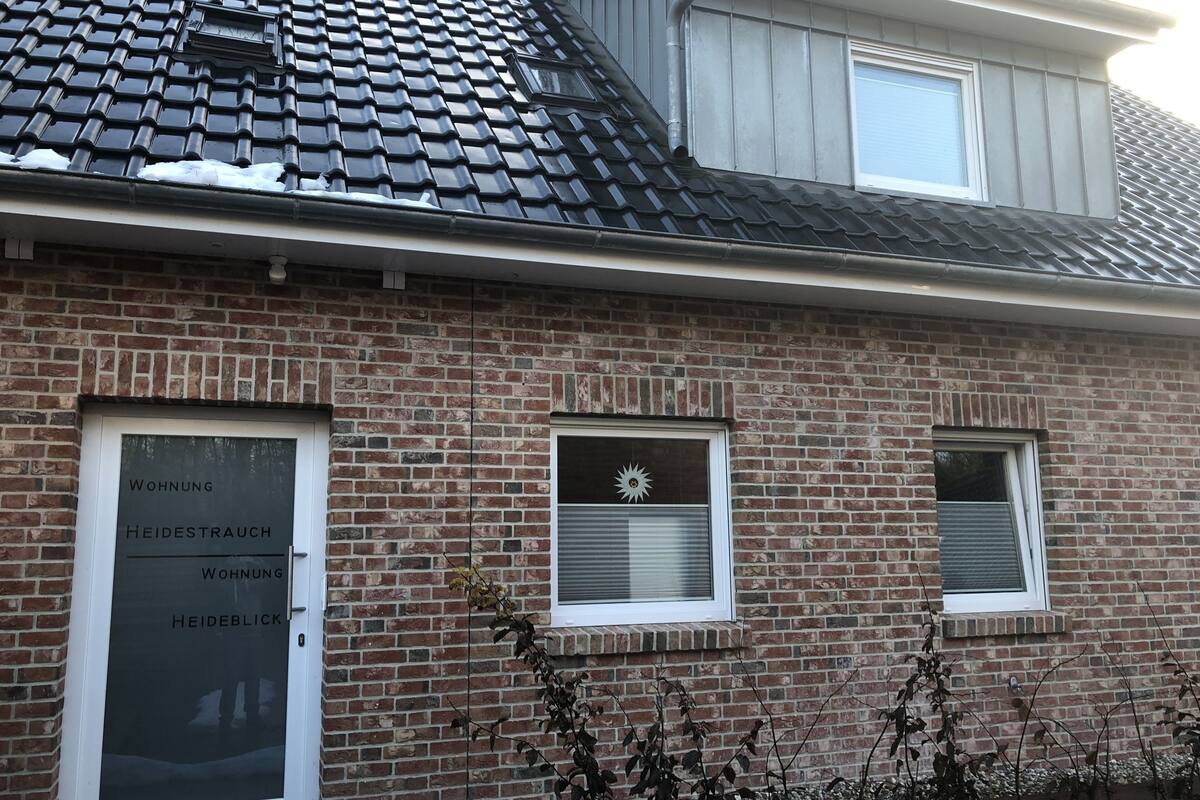 Un bâtiment en briques avec trois fenêtres, dont une ornée d’un autocollant représentant un soleil rayonnant, et une enseigne avec du texte.
