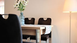 A dining area with a table, chairs, a vase with flowers, a wall clock, and a floor lamp. - Ferienpark Thüle (Friesoythe)