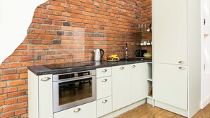 A kitchen with white cabinets, a brick wall, and a black countertop. - Otium Jewish Quarter Miodowa (Kraków)