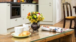 A breakfast setting with a croissant, coffee cups, a vase of flowers, and a newspaper on a glass table. - Otium Jewish Quarter Miodowa (Kraków)
