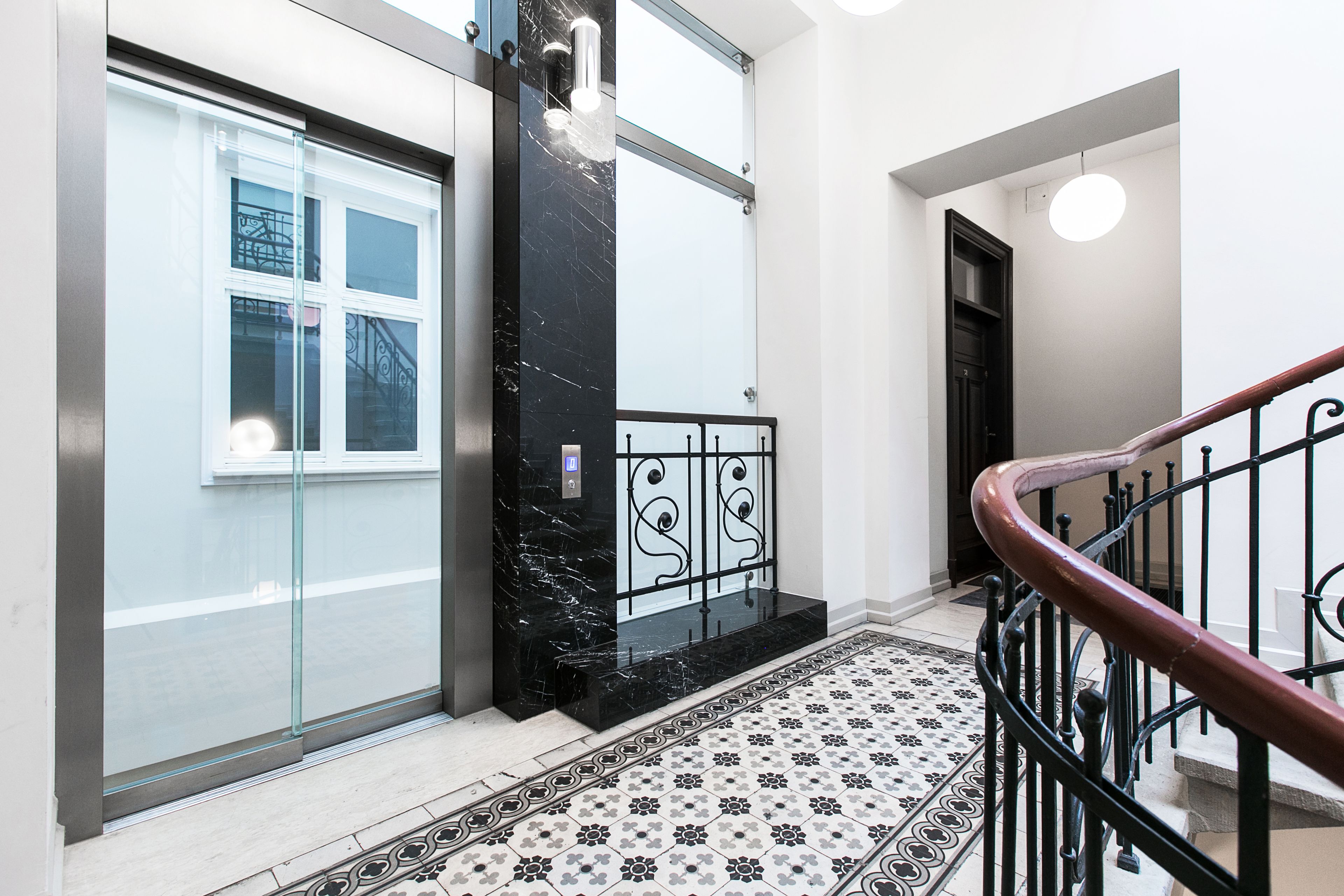 Un intérieur moderne avec un ascenseur en marbre, un sol à motifs et un escalier en métal.