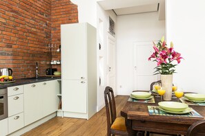 A kitchen with white cabinets, a brick wall, and a dining area with a wooden table set for four. - Otium Jewish Quarter Miodowa (Kraków)