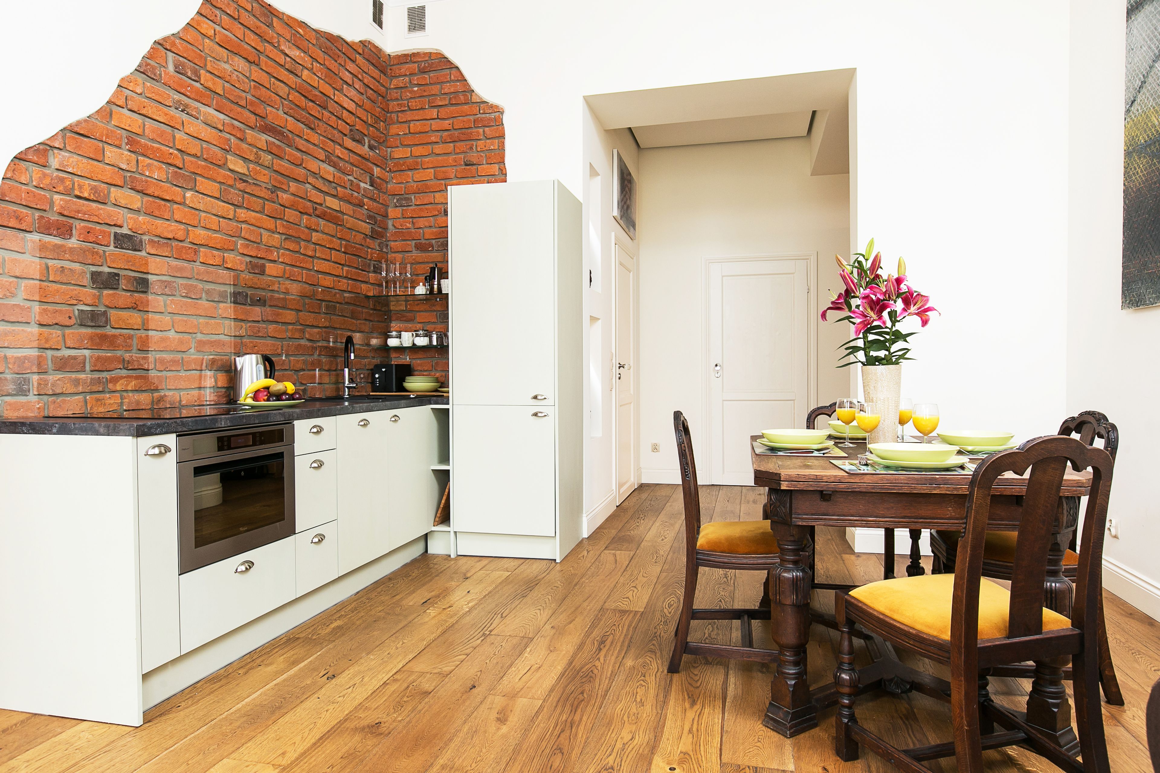 A kitchen with a brick wall, white cabinetry, and a dining area with a wooden table and chairs.