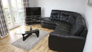 A modern living room with a black leather sofa, a glass coffee table, and a flat-screen TV on a stand.