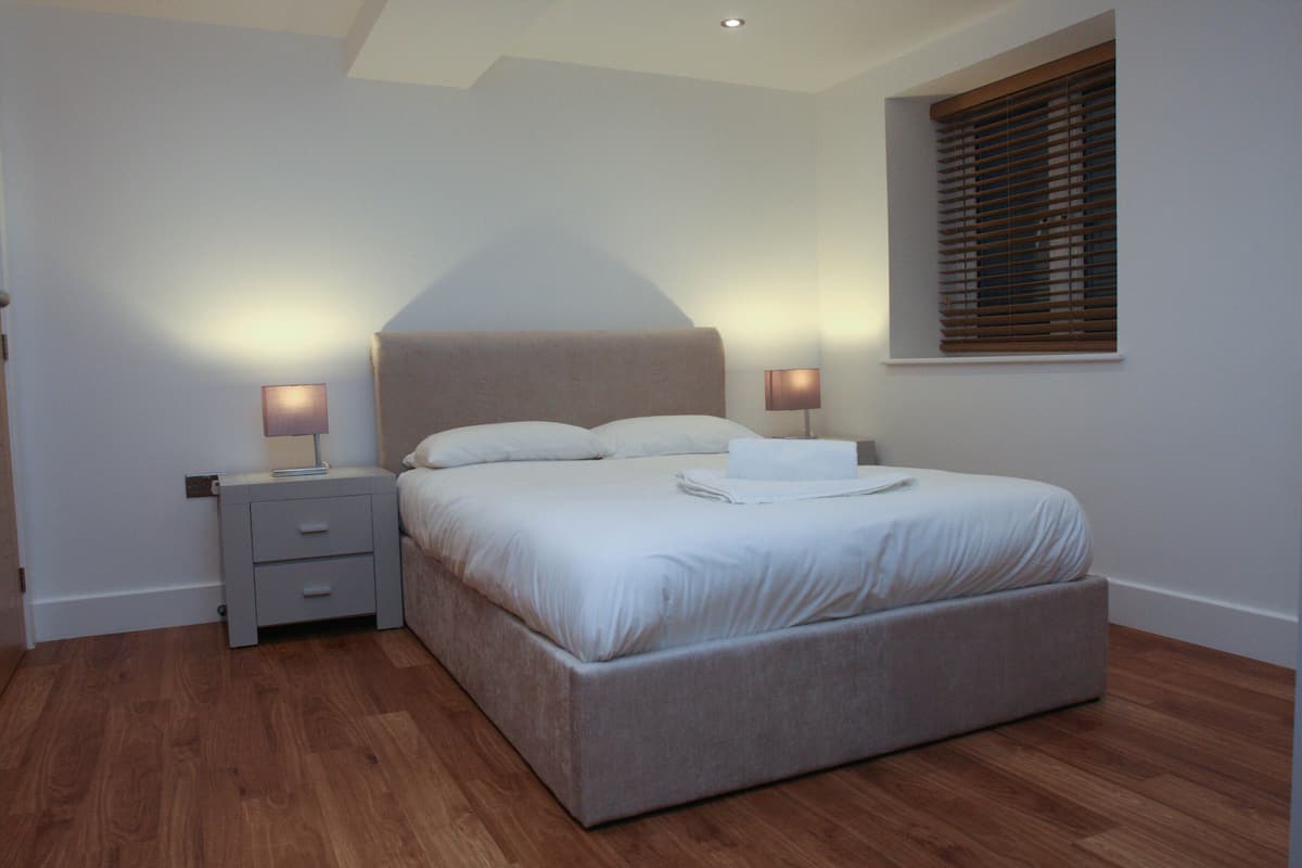 A bedroom with a bed, nightstands, and a window with blinds.