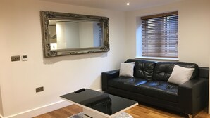 A modern living room with a black leather sofa, a large ornate mirror, and a small white table.