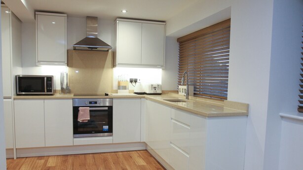 A modern kitchen with white cabinetry, a microwave, an oven, and a window with blinds.