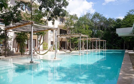 A clear swimming pool with a wooden deck area, surrounded by trees and a building with balconies.