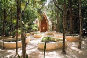 A garden with circular planters and a wooden structure in the background. - Hotel Holistika (Tulum)