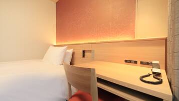 A hotel room with a single bed, a desk with a telephone, and a wall-mounted control panel.