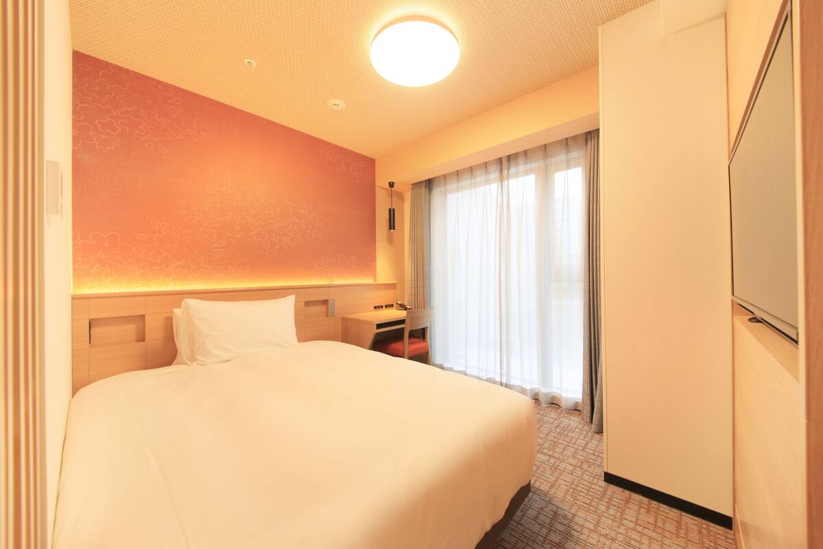 Ein Hotelzimmer mit einem großen Bett, einem Schreibtisch, einem Stuhl, einem Kleiderschrank und einem Fenster mit Vorhängen.