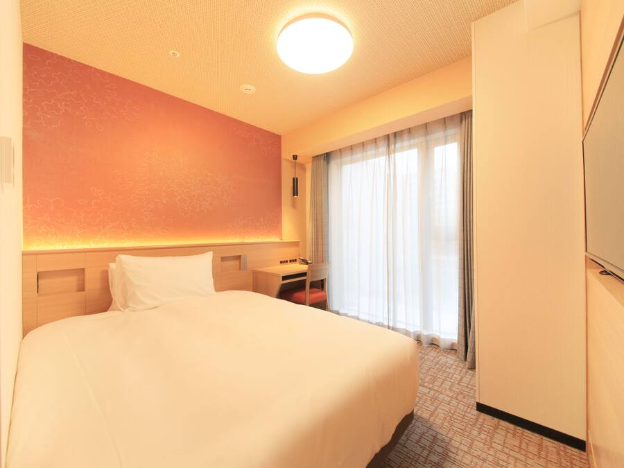 Una habitación de hotel con una cama grande, un escritorio, una silla, un armario y una ventana con cortinas.