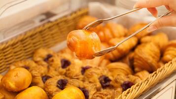 A hand holding a pastry with tongs over a basket of assorted baked goods.