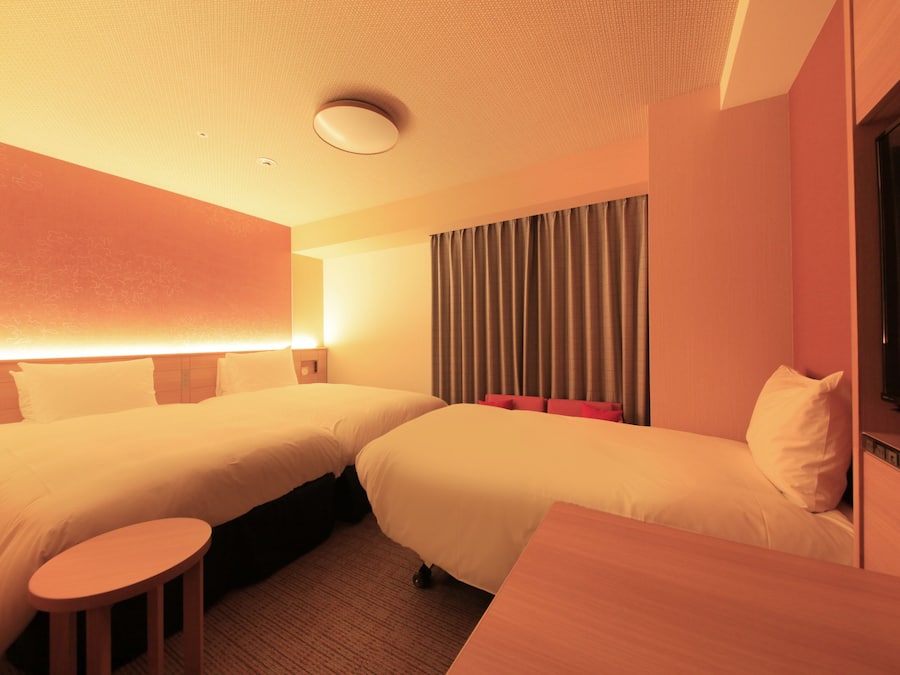 A hotel room with two beds, a small table, a TV, and a curtain.