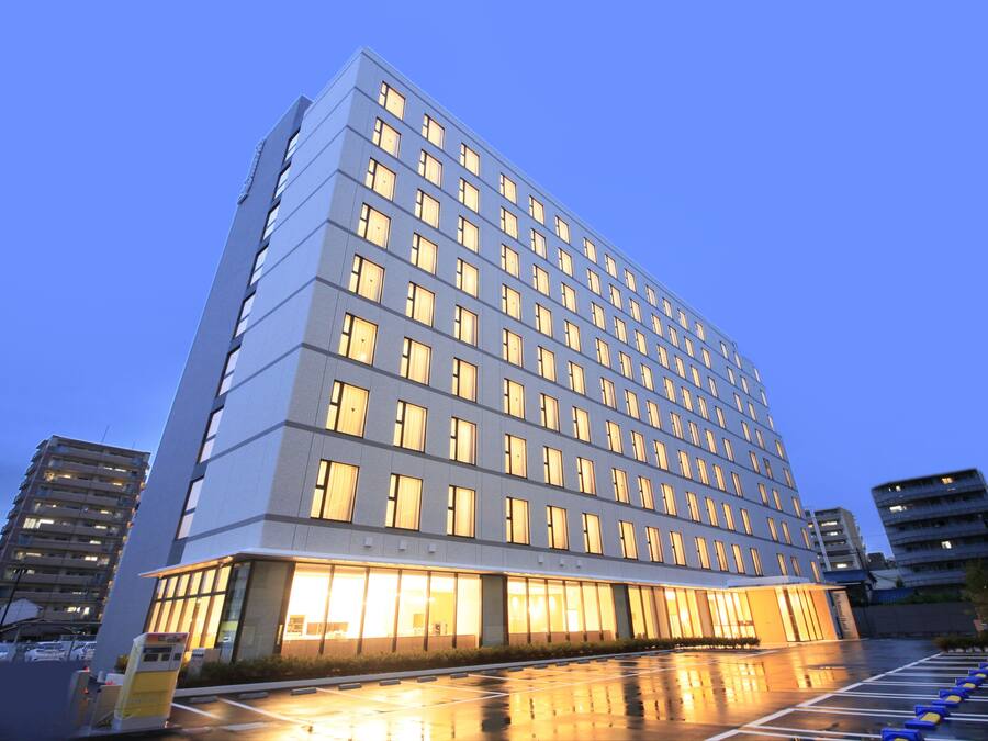 Un hotel de varios pisos con un diseño moderno, con gran cantidad de ventanas y un estacionamiento reflectante.