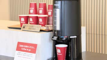 Een koffieapparaat met wegwerpkoffiekopjes en een bordje dat gratis koffie aangeeft.