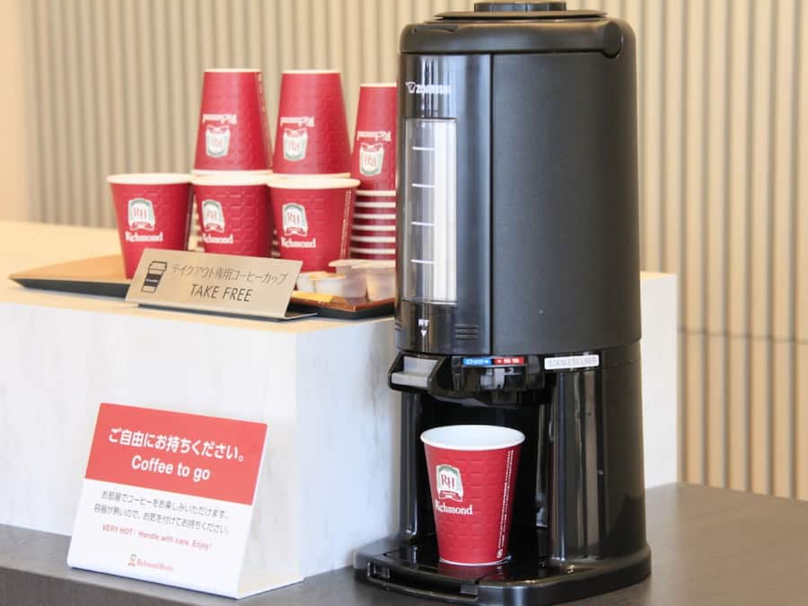 Een koffieapparaat met wegwerpkoffiekopjes en een bordje dat gratis koffie aangeeft.