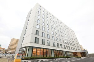 Un hotel su più piani con una facciata moderna, ampie finestre e un'area di parcheggio di fronte.