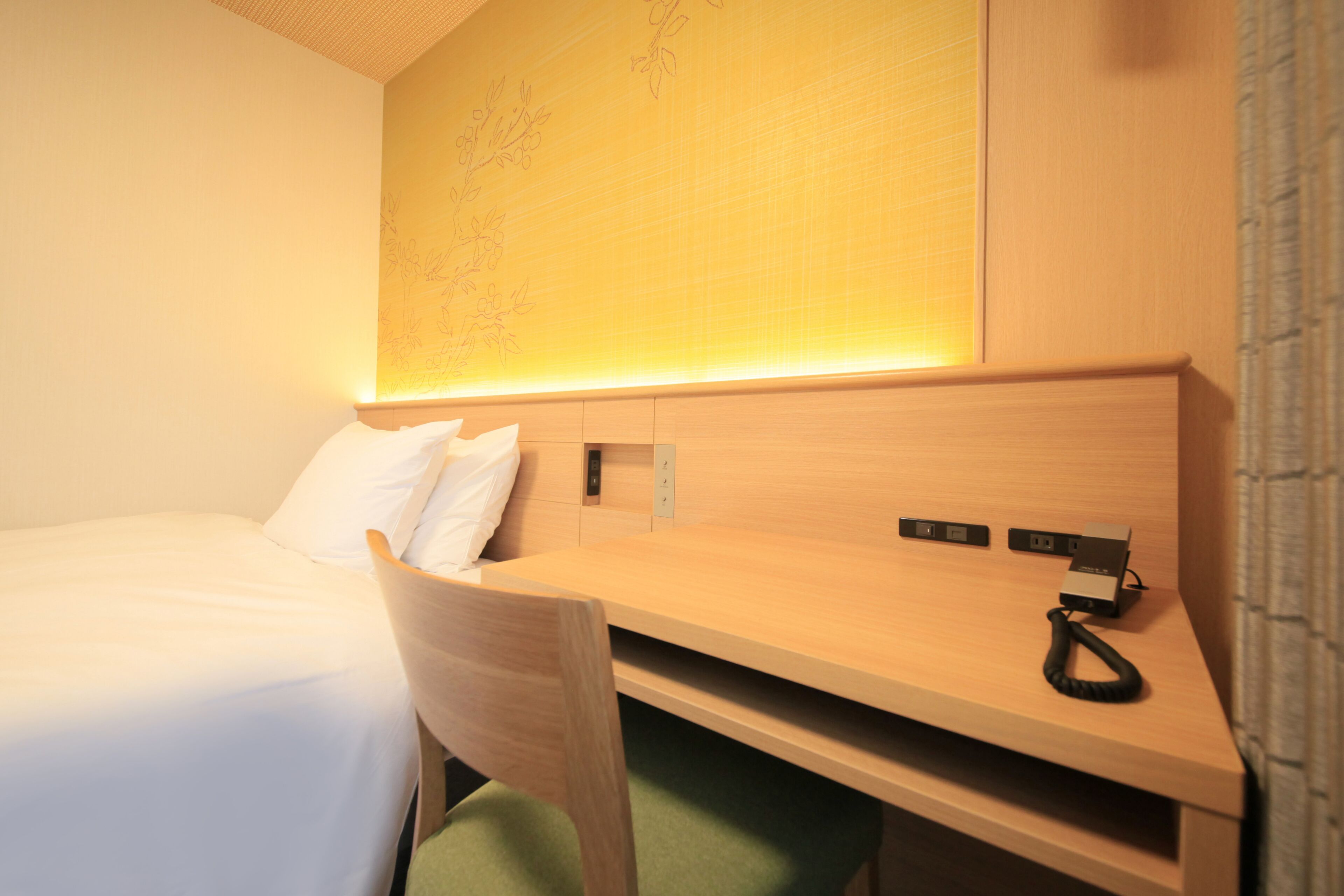 A hotel room with a bed, a desk with a telephone, and a wall-mounted map.