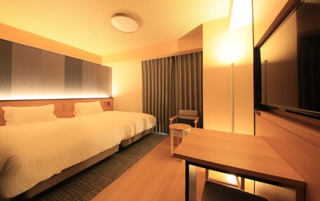 A hotel room with a large bed, a desk, a chair, a TV, and a curtain.