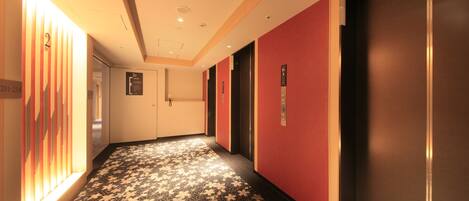 A hotel corridor with patterned carpet, red walls, and elevator doors.