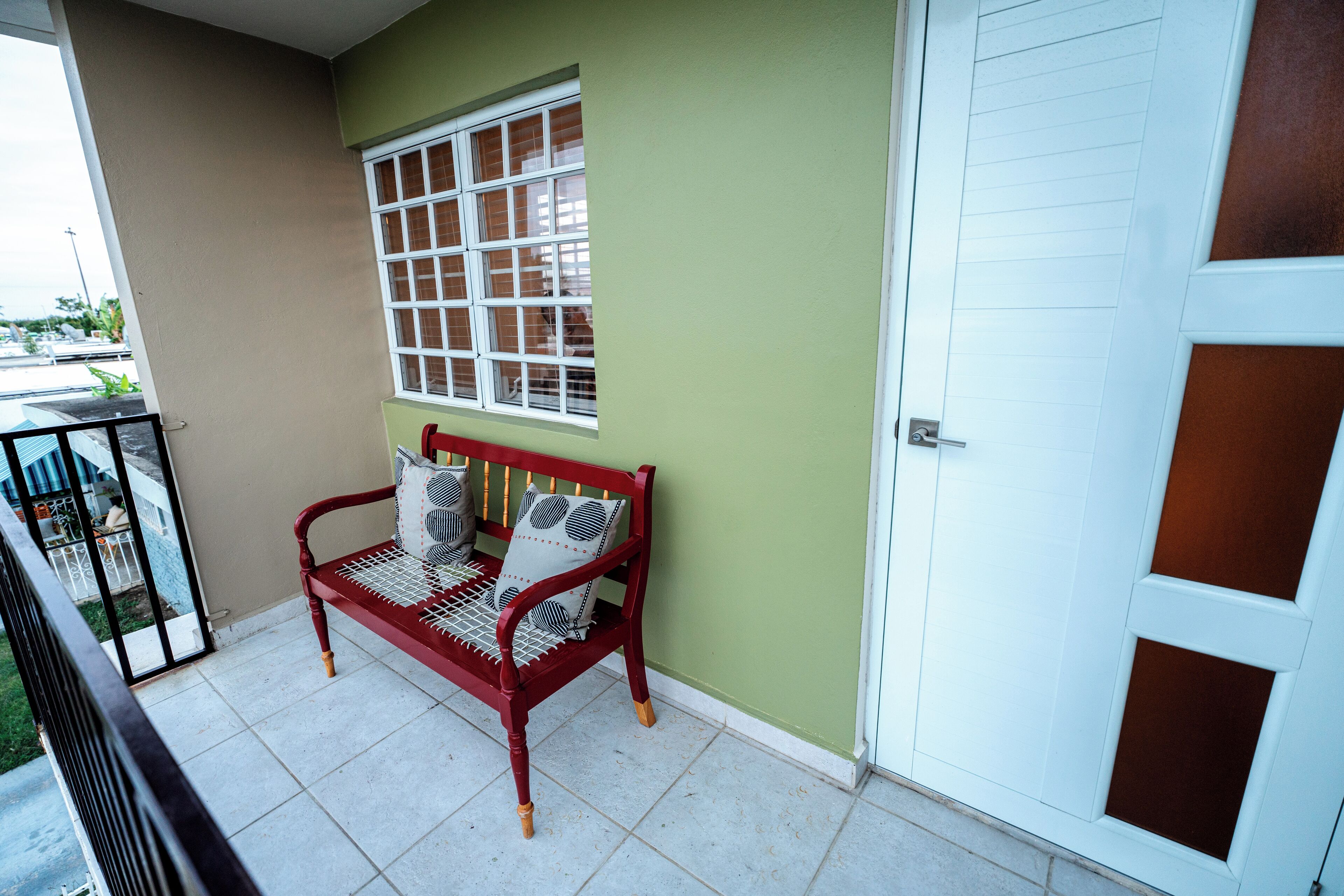A balcony with a red bench, a window with blinds, and a white door.