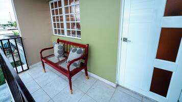 A balcony with a red bench, a window with blinds, and a white door.