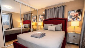 Een hotelkamer met een groot bed, een nachtkastje met een lamp, een spiegel en een raam met gordijnen.