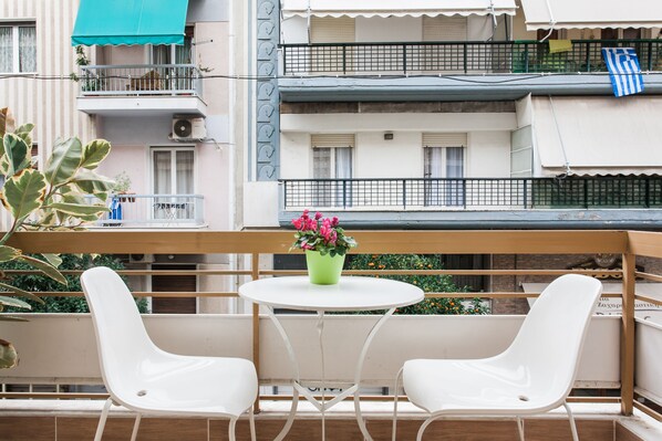 A balcony with two white chairs, a small round table, and a potted plant with pink flowers.