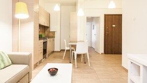 A modern kitchen with white cabinets, a dining area with a white table and chairs, and a wooden door. - Superb under the Acropolis, walking distance to all attractions,  (Athina)