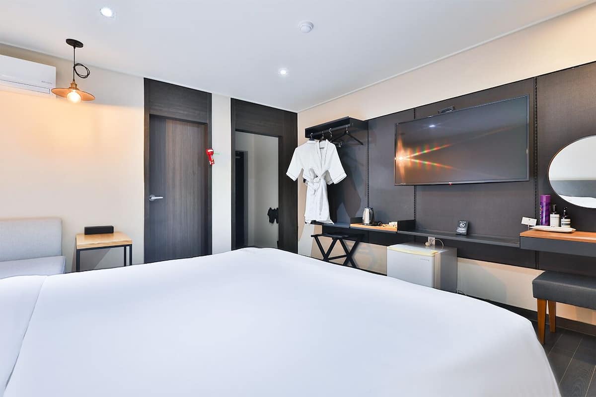 Ein modernes Hotelzimmer mit einem großen Bett, einem Fernseher, einem Spiegel und einem kleinen Schreibtisch mit Pflegeprodukten.