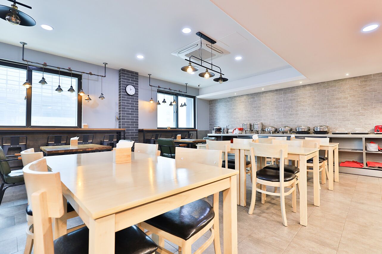 A modern restaurant with wooden tables and chairs, a brick wall, and pendant lighting.