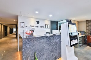 A hotel reception area with a marble counter, a digital information kiosk, and a sign indicating the hotel's name.