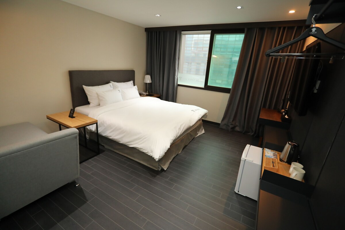 A hotel room with a bed, bedside table, lamp, and a small seating area.