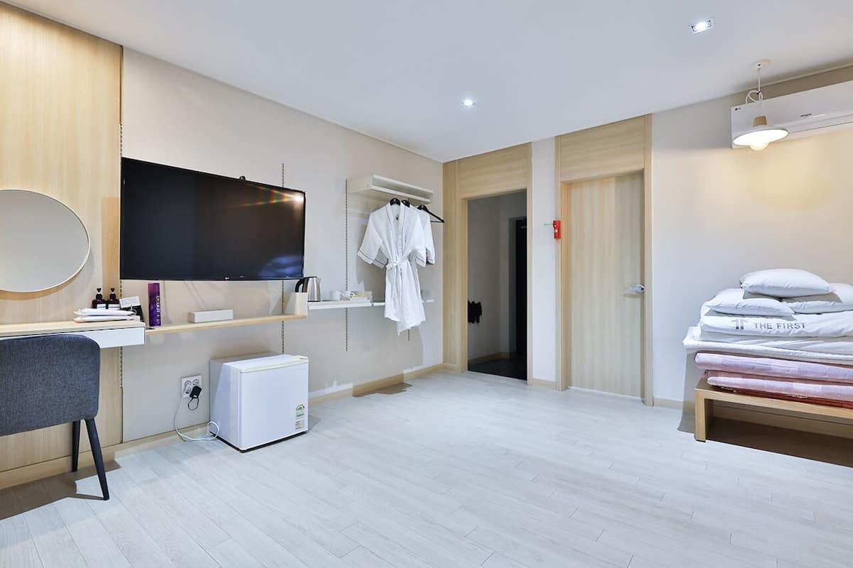 Ein modernes Hotelzimmer mit Flachbildfernseher, Schreibtisch mit Stuhl, einer Minikühlschrank, einem Bett mit Kissen, einem Bademantel und einem Kleiderschrank.