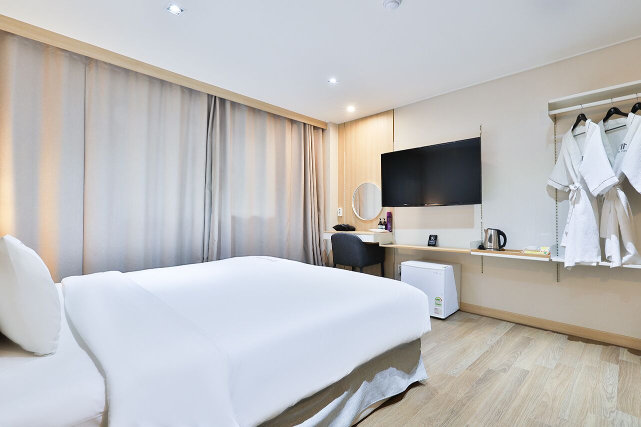 Habitación de hotel con una cama grande, un escritorio con televisor de pantalla plana, un espejo y un estante con batas y artículos de aseo.